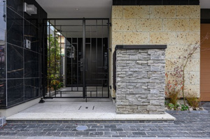 【玄関】 | 重厚感のある石貼り壁とアイアン調の門扉が、住まいの風格を物語るエントランス。夜間も明るい照明が足元を照らし、家族を温かく迎え入れます。洗練されたデザインが、帰宅するたびに心地よい満足感を届けます。