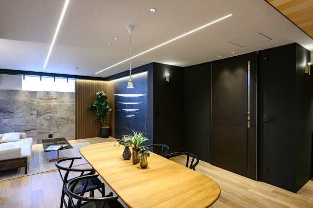 【居間・リビング】 | 質感の異なる壁材を組み合わせた、デザイン性の高い内装。窓の外にはバルコニーが広がり、柔らかな光が差し込みます。30畳超の広さを活かして、大型の家具もゆとりを持って配置できる自由度の高さが魅力です。