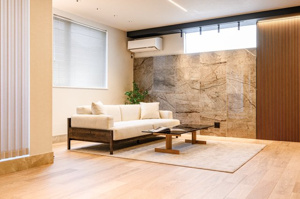 【居間・リビング】 | 大判タイルのアクセントウォールと、柔らかな木目のフローリングが調和する開放的なLDK。高窓から光が差し込み、外からの視線を遮りつつ明るさを確保。ソファで寛ぐ家族の時間を、より豊かに演出する空間です！