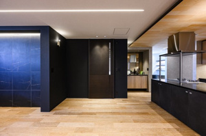 【居間・リビング】 | 落ち着いたダークトーンの建具と、温かみのあるフローリングが調和したリビング。間接照明が壁面の質感を浮き上がらせ、奥行きのある空間を演出します。家族がゆったりとくつろげる、上質なインテリアです。