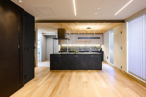 【居間・リビング】 | 空間を広く使えるアイランド型キッチン。作業動線がスムーズで、複数人での料理も楽しめます。木の温もりを感じる天井とモダンな黒のコントラストが美しく、毎日の家事時間がクリエイティブなひとときに！