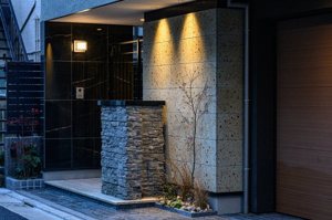 【玄関】 | ライトアップされた石目調の壁面が、夜の街並みに美しく映える外構デザイン。陰影が素材の表情を豊かに描き出し、住まいの気品をいっそう際立たせます。夜遅い帰宅時も、この明かりが安心感をもたらします。