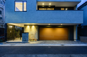 【外観】 | シャープなラインが際立つモダンな外観。電動シャッター付の車庫は、夜間でも美しくライトアップされ、大切なお車を雨風から守ります。プライバシーに配慮された落ち着きのある佇まいで、家族の時間を育みます。