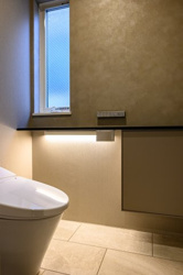 【トイレ】 | 質感にこだわった壁面と、足元を優しく照らす間接照明が、清潔感と安らぎを両立。小窓からは自然光が入り、日中も明るく爽やかな印象です。生活感を感じさせない収納棚も備え、細部まで配慮が行き届いています。