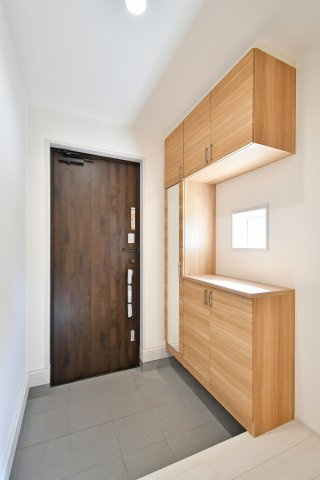 上尾市原市全1棟　1号棟の玄関|シックな色合いの玄関ドアが家族を優しく迎えます。トールタイプのシューズボックスは、大容量の収納力に加え、お出かけ前の身だしなみチェックに便利な姿見付き。小窓からの柔らかな光が空間を明るく演出します。