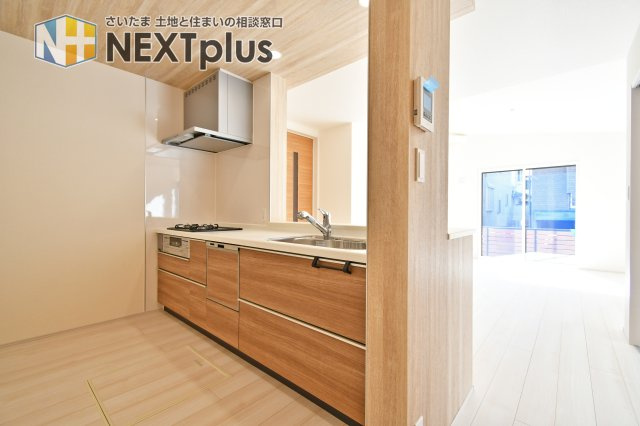 上尾市原市全1棟　1号棟のキッチン|リビング全体を見渡せる対面キッチンは、家族との会話が弾む特等席。木目調の美しいデザインに、家事を支える食器洗浄乾燥機も完備。勝手口や収納も備え、デザインと機能性が両立した理想の調理空間です。