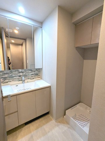 SEASON FLATS新御徒町EASTの洗面所|トイレと独立した洗面室に洗濯機置場、三面鏡・ハンドシャワー付洗面台、洗面台の下にヘルスメーターストックあり、洗濯機置場は排水口のお手入れしやすい様に手前に配置した防水パンです