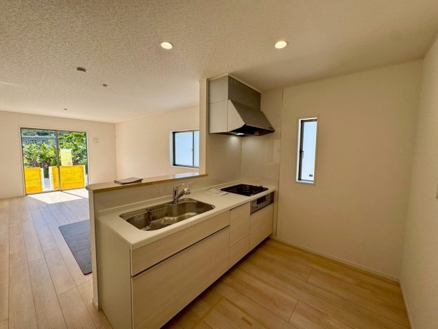 クレイドルガーデン南城市佐敷佐敷 第1・２号棟のキッチン|会話の弾む対面式のシステムキッチン・換気窓＆床下収納付き／キッチンからリビングの眺め