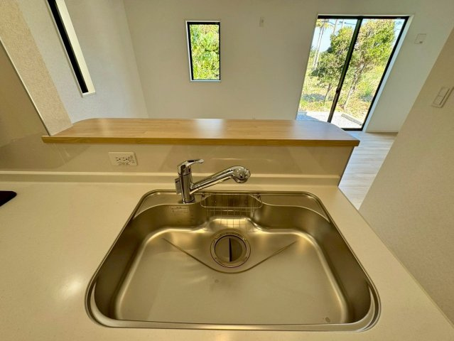 クレイドルガーデン南城市佐敷佐敷 第1・３号棟のキッチン|浄水器付きキッチンの流し台／リビングの眺め