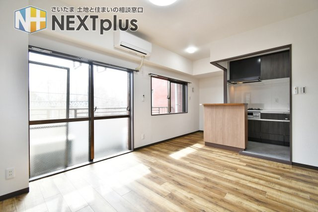 光建ハイムブリリアンス大宮公園の居間・リビング|バルコニーから暖かな陽光が差し込む、明るいリビング空間。木の温もりを感じるフローリングと白壁が清潔感を演出します。キッチンには便利なカウンターを配し、和室を繋げて広々と開放的に活用することも可能です。