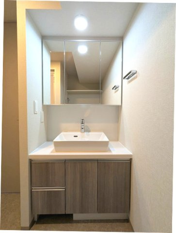 URBANEX上野の洗面所|トイレと独立した洗面脱衣室、三面鏡付洗面台、左下にヘルスメーターストックあります、洗濯機置場は大型ドラム式も配置しやすいスペース確保し、排水口のお手入れしやすい様に手前中央に配置し、足高の防水パンです