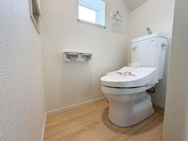 細第1-2号棟のトイレ|清潔感のあるシンプルなトイレ空間です。小窓付きで換気ができ室内が明るい印象です。床はナチュラルな木目調で落ち着いた印象です。