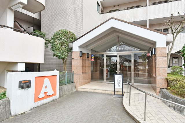 ベルヴィル大宮A棟|重厚感あるタイル貼りと、手入れの行き届いた植栽が迎えるエントランス。スロープ完備のバリアフリー設計で、ベビーカーやペットとの移動もスムーズです。管理体制の良さが一目で伝わります。