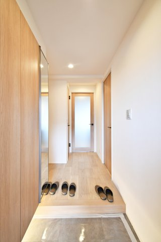 ベルヴィル大宮A棟の玄関|一歩足を踏み入れれば、木の温もりと柔らかな間接照明がお出迎え。大型の姿見や新規交換済みの下駄箱を備え、機能性も追求しました。デザイン性と利便性が融合した、住まいの顔に相応しい空間です。