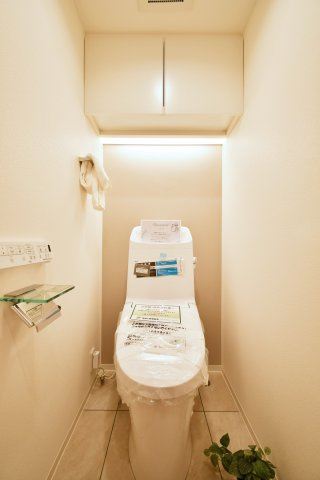 ベルヴィル大宮A棟のトイレ|清潔感あふれる温水洗浄機能付きトイレに新規交換済み。吊戸棚でストック品もスッキリ収納できます。落ち着いたアクセントクロスが、家族がホッと一息つけるプライベート空間を演出します。