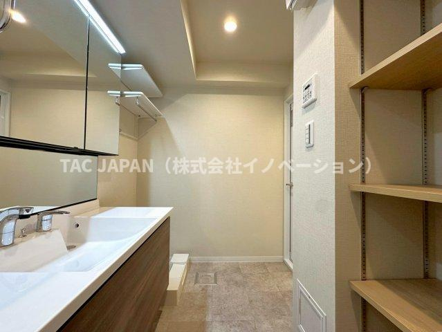 サンクレイドルレヴィール池袋の洗面所|大型の洗濯機を置いても余裕が感じられる脱衣スペースにはお洒落な洗面ユニットを制作。着替えやタオル、洗剤の買い置きなどリネン庫の使い方はお客様しだい。