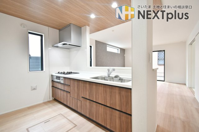 伊奈町小室10期　全1棟のキッチン|料理中もリビング全体を見渡せるオープン設計。木目調の天井と扉が調和したモダンなデザインです。床下収納や窓もあり、明るく機能的。家族との会話を楽しみながら、軽やかに家事をこなせる理想の空間。