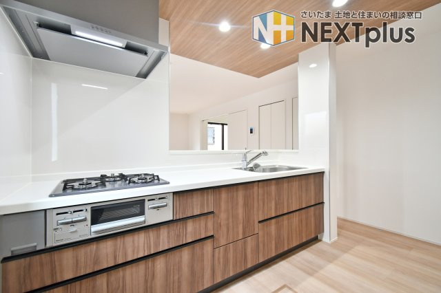 伊奈町小室10期　全1棟のキッチン|お手入れ簡単な三口コンロとワイドな天板を採用。スライド式の引き出し収納は奥の物まで取り出しやすく、家事効率が格段にアップします。白と木目のコントラストが美しい、洗練されたキッチン。