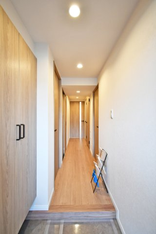 クレセント東鷲宮の玄関|玄関扉を開けると、リノベーションにより白を基調とした明るく開放的な廊下が広がります。突き当たりのLDKから差し込む光が奥行きを演出し、毎日の外出や帰宅を心地よく彩る、住まいの品格を感じる意匠です。