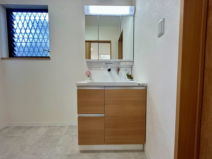 松山市西長戸　再生住宅の独立洗面台|清潔感あふれる新品の洗面化粧台を設置。三面鏡の裏など収納も充実しており、散らかりがちな洗面小物もすっきり片付く。広めの脱衣スペースで、お風呂上がりの着替えや洗濯もスムーズに。