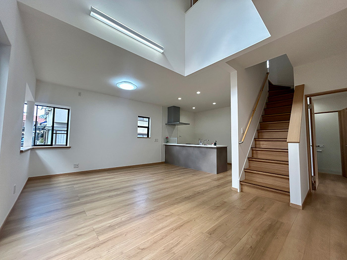 松山市西長戸　再生住宅の居間・リビング|吹抜けから光が降り注ぐ18帖以上のLDK。リフォームで壁紙も床も新しくなり、開放感たっぷりの空間に。家族が自然と集まりたくなる、心地よい風が吹き抜けるような住まいの中心。