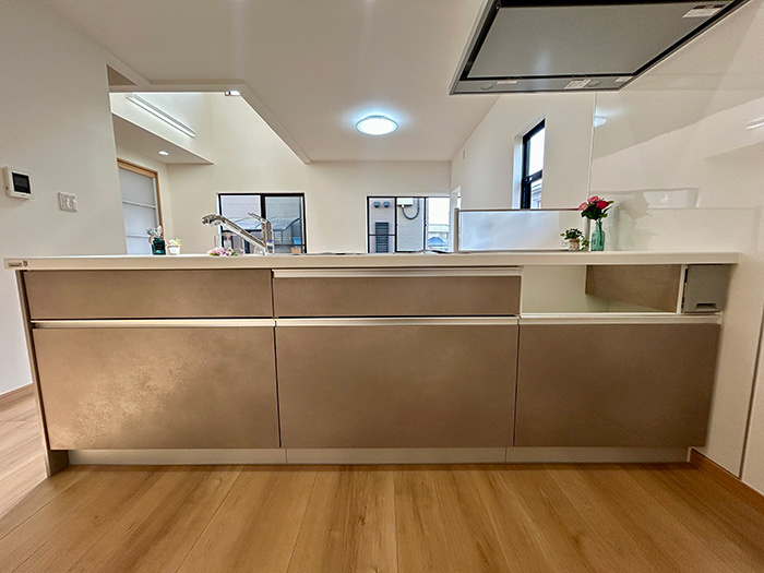 松山市西長戸　再生住宅のキッチン|新品の対面式システムキッチンを採用。リビングを見渡しながらお料理ができるから、お子様との会話も弾む。3口コンロで時短調理が叶い、できたての料理をすぐに食卓へ運べる、家族想いの設計。