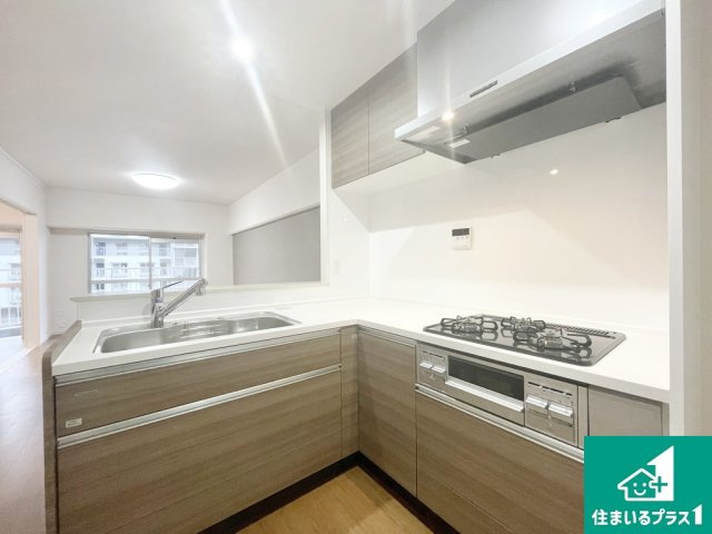 エバーグリーン金岡四号棟のキッチン|フローリングと統一したブラウン調のＬ字型キッチンです！リビングを見渡せる上、ワークトライアングルが短くなるため、少ない歩数で効率よく料理ができます！【現地写真】