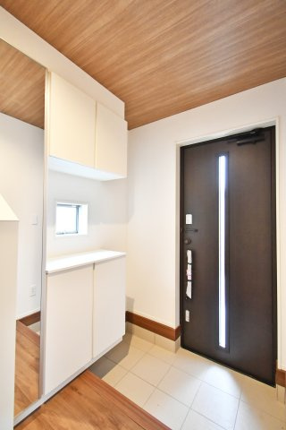 蓮田市西新宿11期　全1棟の玄関|大型のセパレート型収納を備え、家族の靴もスッキリ片付きます。身だしなみをチェックできる姿見や、自然光が差し込む小窓付き。シックな木目調の天井が、心地の良いお出迎えを演出します。