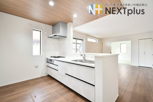 蓮田市西新宿11期　全1棟のキッチン|料理中もリビングの家族と会話が弾む対面式。木目調の天井が空間にメリハリを与え、洗練された印象に。広々とした天板と勝手口代わりの小窓で、家事効率も格段にアップします。