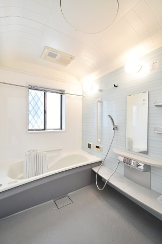 伊奈町西小針1丁目の浴室|浴室乾燥機付きで雨の日の洗濯も安心。窓からの自然光が心地よく、換気もスムーズです。ゆったり浸かれる浴槽と手すり付きの安心設計。清潔感のあるブルーのパネルが、爽やかでリラックスできる空間を演出します。