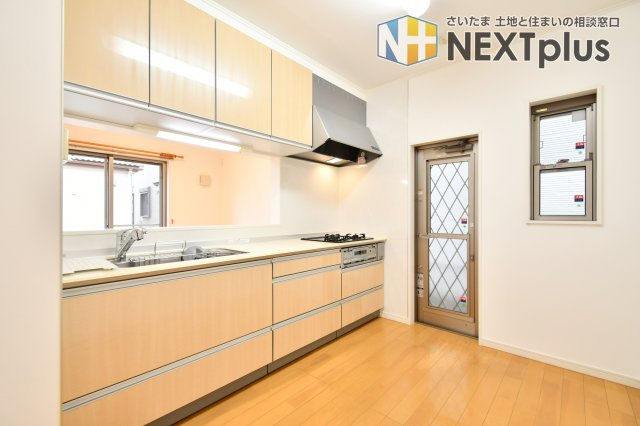 伊奈町西小針1丁目のキッチン|明るい木目調のデザインが清潔感を演出。勝手口付きでゴミ出しや換気もスムーズです。大容量の上下収納を備え、調理器具もスッキリ片付きます。窓からの自然光を感じながら、毎日の料理をより楽しく軽快な時間に。