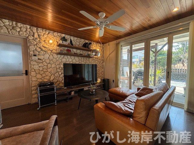 藤沢市鵠沼海岸1丁目　中古戸建の居間・リビング|木天井×オーシャンストーンの壁面が印象的な17帖LDK。
カバードポーチへと続く大開口が、湘南の光と風を室内へ取り込みます。
