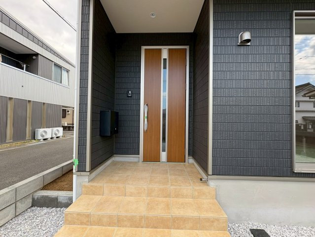 香美市土佐山田町東本町第1　1号棟新築戸建ての玄関|重厚感ある外壁に木目玄関ドアが映えるエントランス。屋根付きポーチで、雨の日の出入りも安心です。