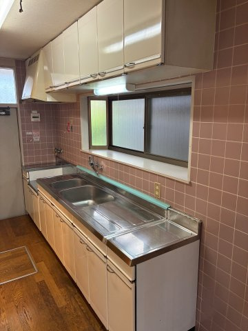 桃山台5丁目中古戸建のキッチン|壁付けタイプのキッチンは、窓からの明るい光の中で効率よくお料理を楽しめます！レトロな雰囲気のタイル壁がお洒落で、上下の収納棚には調理器具や食器もしっかり収まります。毎日の食事作りが捗る機能的な設計