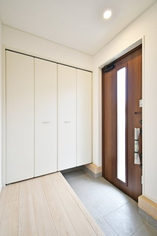 伊奈町本町第3　全2棟　1号棟の玄関|家族全員の靴をすっきり収める大型収納を採用。フロートタイプのため足元に空間があり、玄関を広く見せる効果も。木目調のドアから差し込む光が、明るく清潔感あふれる「家の顔」を演出します。