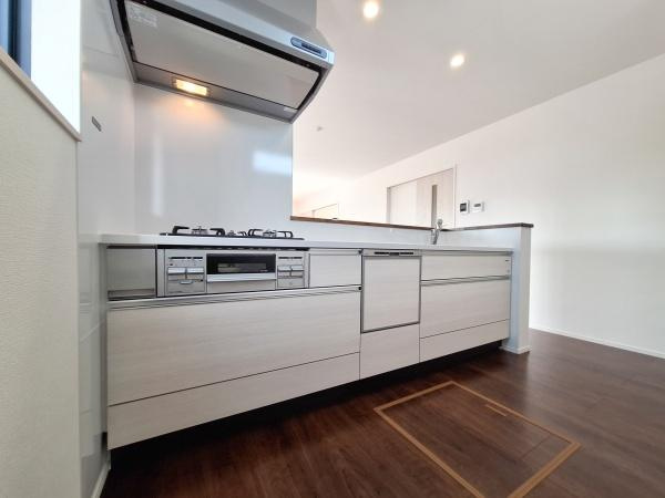 花高松2丁目1期1号棟のキッチン|キッチンは引き出し収納が充実していて調理器具や食器もすっきりと整理できます。ガスコンロやシンクが並び作業がしやすいレイアウトです。白を基調としたデザインと木目調の床が清潔感を演出しています。