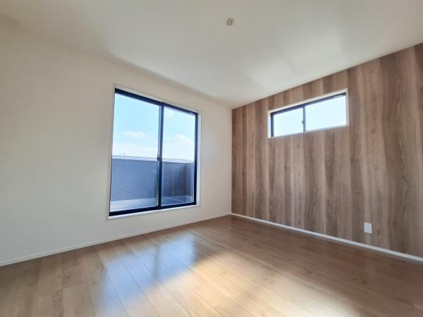 大字佐野1期3号棟の洋室|大きな窓から自然光がしっかりと入りリビングが明るい印象です。木目調のアクセントクロスが空間を引き締めています。床材もナチュラルな風合いで統一感があります。