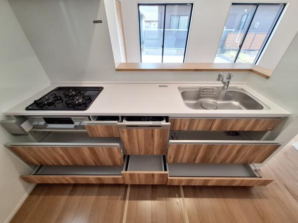 大字佐野1期3号棟のキッチン|木目調の引き出しが採用されているキッチンです。収納スペースが充実しており整理しやすい構造になっています。シンクとコンロがすっきりと並び作業動線に配慮されています。