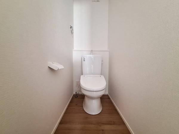 大字佐野1期2号棟のトイレ|シンプルで清潔感のあるトイレ空間です。壁と床の配色が落ち着いた雰囲気を演出しています。ペーパーホルダーも使いやすい位置に設置されています。手入れがしやすいシンプルなレイアウトです。