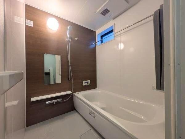 タマタウン横尾東町2　2号地の浴室|落ち着いた木目調パネルが印象的なバスルームです。ゆとりのある浴槽で毎日の利用に適しています。窓付きでしっかり換気ができます。明るい照明が空間を照らし清潔感を感じられる仕様です。