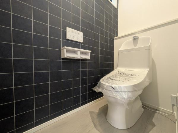 タマタウン横尾東町2　2号地のトイレ|落ち着いた色合いのタイル壁で洗練された印象のトイレ空間です。新しい設備が設置されており清潔感が漂います。