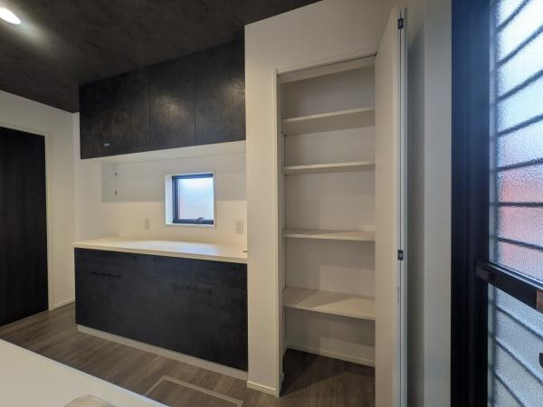 タマタウン横尾東町2　2号地のキッチン|収納スペースが充実したキッチンエリアです。窓があるため採光も期待できます。シックな色合いの建具が空間に落ち着きを与えています。パントリーも備わっており整理整頓がしやすい設計です。