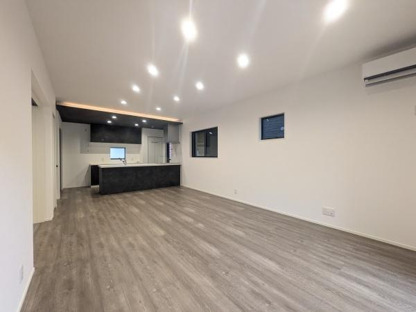 タマタウン横尾東町2　2号地の居間・リビング|リビングは広々とした空間が広がり明るい照明が室内をしっかり照らしています。床材は落ち着いた色合いで統一されモダンな印象を与えます。天井のダウンライトが奥行きを感じさせる仕上がりです。