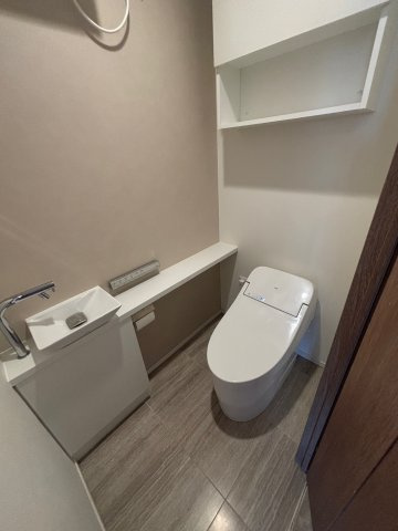 【清潔感溢れるトイレ】手洗いカウンター付きのタンクレストイレを採用し、スッキリとした空間に。上部には収納棚も完備しています。落ち着いた色調の内装が、プライベートな時間に安らぎを与えてくれます。