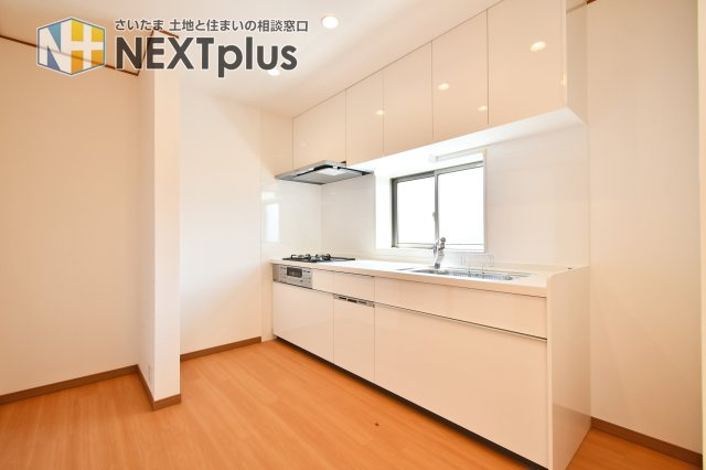 さいたま市見沼区深作2丁目のキッチン|白を基調とした清潔感あふれるシステムキッチン。背後には冷蔵庫やカップボードを置いても余裕のある広々としたスペースを確保しました。明るい木目調の床が、毎日の料理時間を心地よく彩ります。