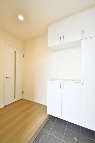 第17上尾上　全6棟　B号棟の玄関|横幅にゆとりを持たせた玄関スペースは、買い物帰りや小さなお子様との出入りもスムーズ。木目調のフロアと黒のタイルが織りなすモダンなコントラストが、ワンランク上の住まいを感じさせる洗練された空間です。