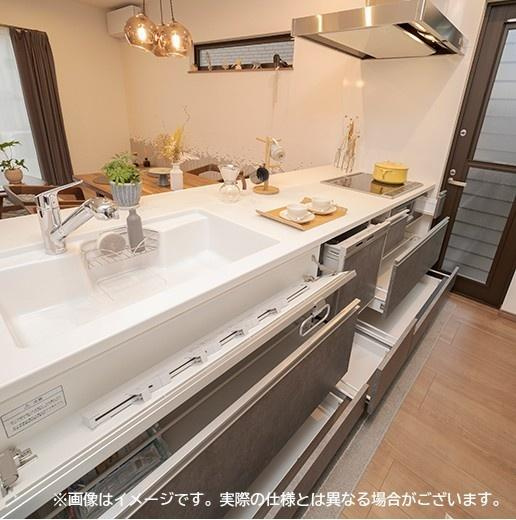 大在汐見　A棟のキッチン|シンクや作業スペースが広く設けられており効率的な調理環境が整っています。収納力のある引き出し式収納で片付けもスムーズです。室内全体が明るく家事の動線にも配慮されています。