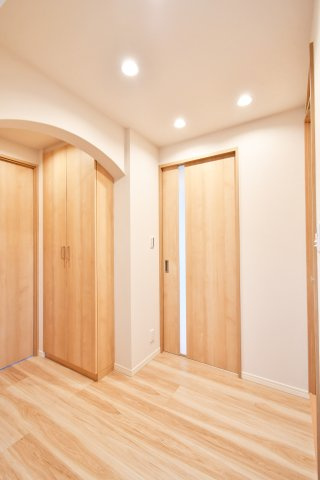 ソフィア上尾C棟の玄関|アーチ壁が目を引く玄関ホールは、意匠性と収納力を両立。大型シューズボックス付きで、家族全員の靴もスッキリ収まります。温もりある木目調の建具が、リビングへ続く期待感を高めるリノベならではの設計です。