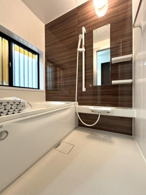 【浴室】 | 草加市青柳6丁目・戸建 | 木目調のパネルが空間に落ち着いた印象を与えます。大きな窓が採光を確保し明るい雰囲気になっています。掃除のしやすいフラットな床面が特徴です。収納棚やミラーも使いやすい配置です。
