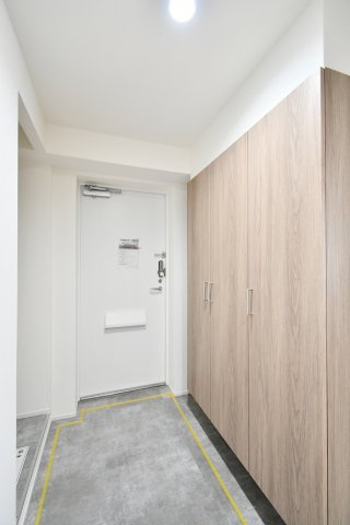 グリーンパーク大宮1号棟の玄関|玄関を開けた瞬間洗練された木目調の大型シューズボックスがお出迎え。天井まで届く大容量の収納力で、家族全員の靴をスッキリ整理できます。リノベーションによる清潔感溢れる空間が、住まいの第一印象を高めます。